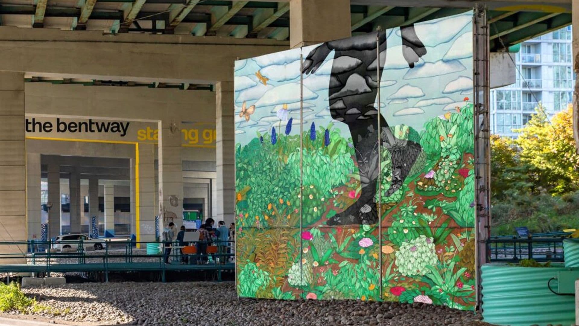 Vibrant mural under The Gardiner, depicting a large black silhouette walking through a colorful garden scene, with people nearby.